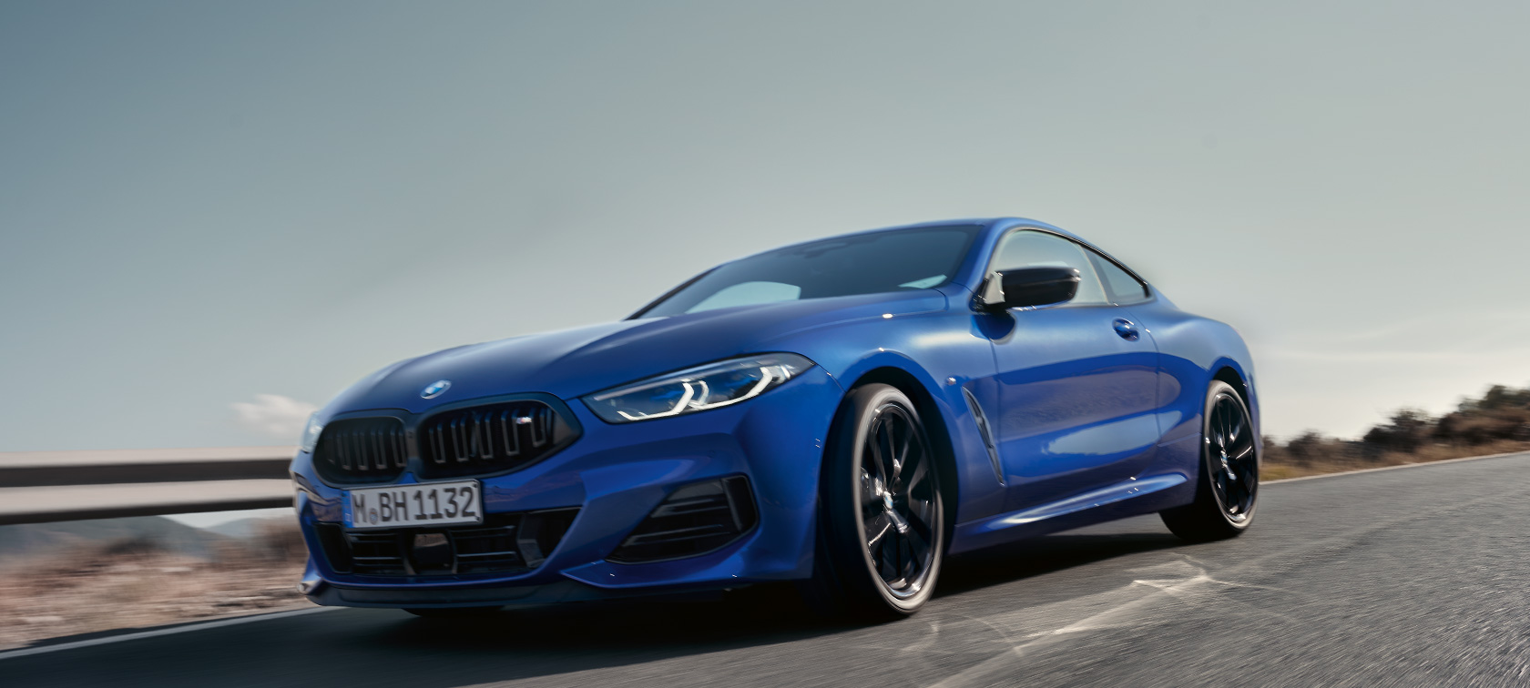 The BMW 8 Series Coupé G15 LCI Facelift 2022 BMW M850i xDrive M Portimao blue metallic front view low-angle shot driving on country road in with hills in the background 